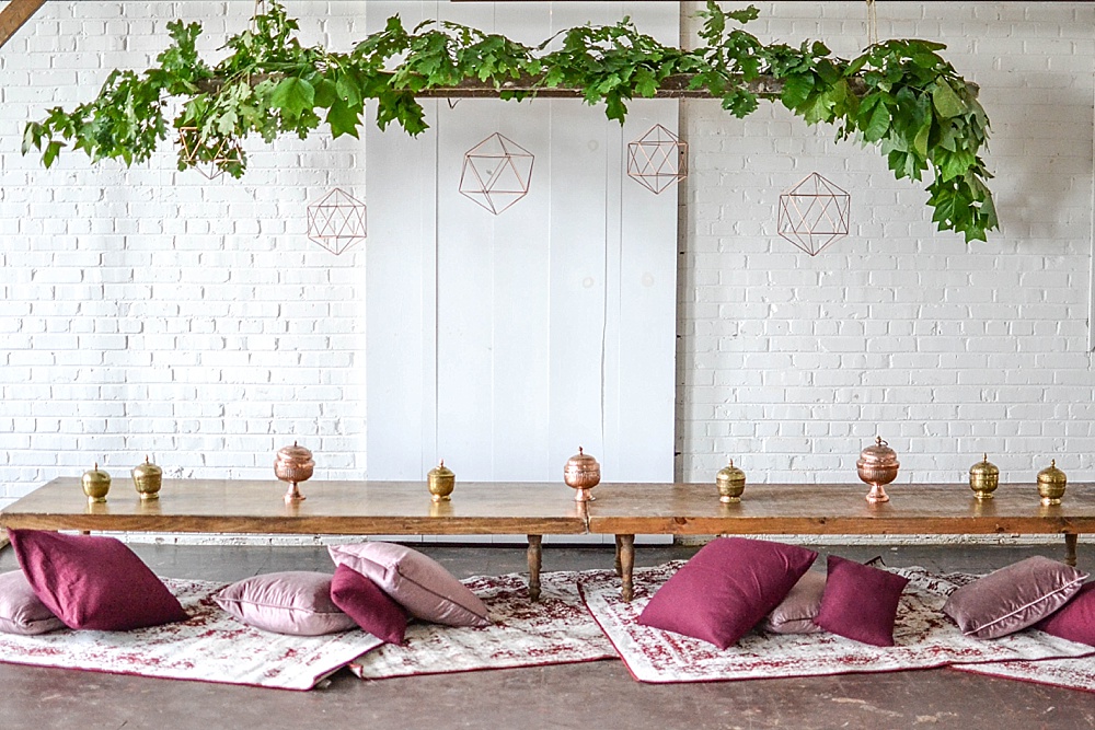 Gorgeous boho dining setting with wooden truss, copper accents, rugs low-set tables and pillows at highpoint and moore by Paisley and Jade