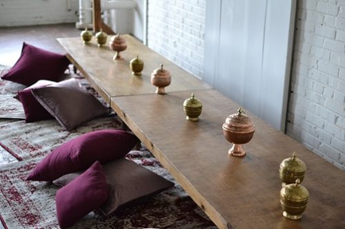 Gorgeous boho dining setting with wooden truss, copper accents, rugs low-set tables and pillows at highpoint and moore by Paisley and Jade